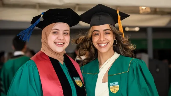 Two women wearing graduation regalia smile to the camera
