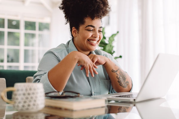 A smiling person sitting at a desk looking at a laptop screen