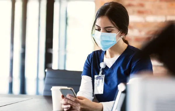 A healthcare worker wearing scrubs sits in a cafe using a phone
