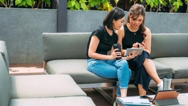 Two women seated outdoors look at a phone screen together