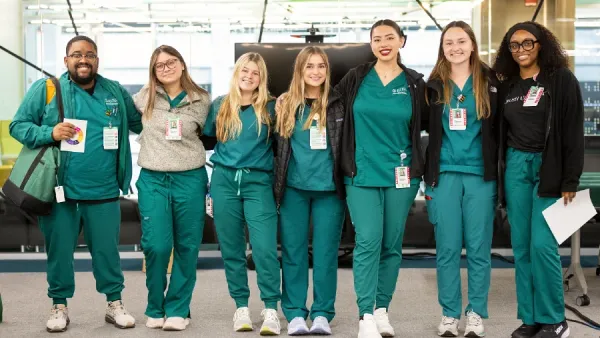 A group of nursing students wearing scrubs stand together smiling
