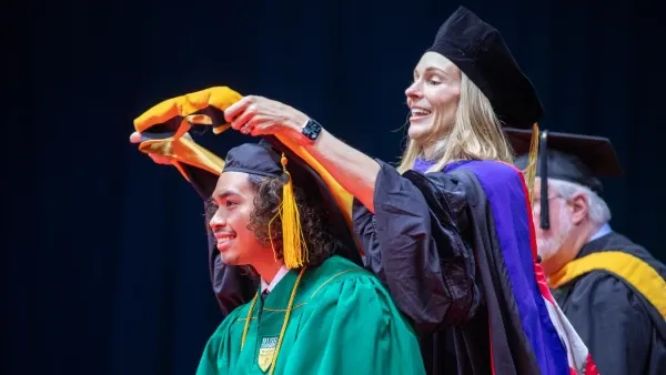 A faculty member places a sash around a graduating student's gown