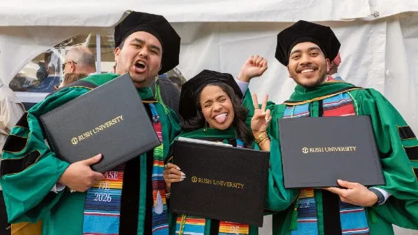Three students wearing graduation robes and holding diplomas, smiling happily