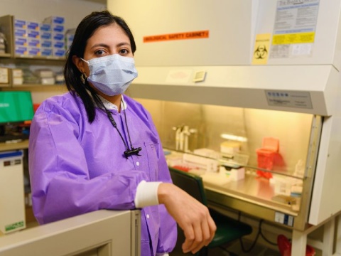 A scientist wearing protective gown and mask faces the camera in a research lab