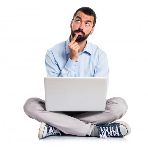 Man thinking sitting cross legged with a laptop on his lap 
