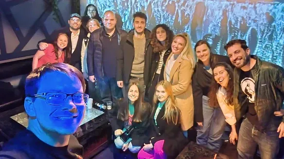 A group of people standing together and smiling in a cozy room in front of a projection screen