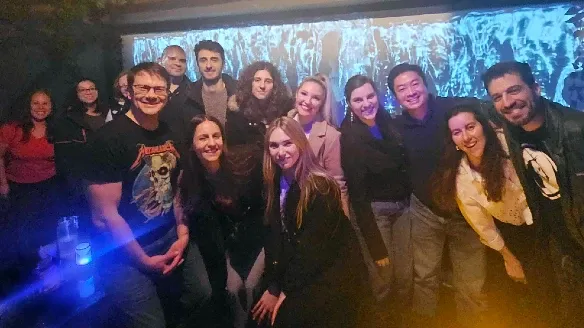 A group of people standing together and smiling in a cozy room in front of a projection screen