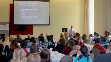 A conference room with people seated at tables facing a lecturer at a podium