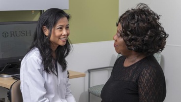A health care provider wearing a white coat speaks with a patient