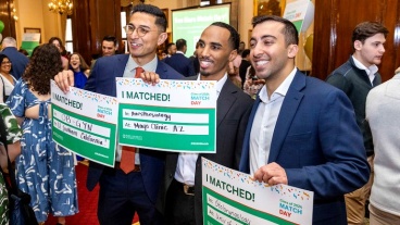 Three students in a crowded room, smiling and holding signs with the words I Matched