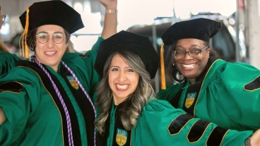 Three people wearing graduation regalia pose and smile for the camera