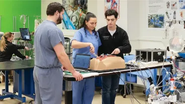 Three students demonstrating a procedure on a medical mannikin