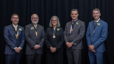 Five faculty members wearing medals stand together