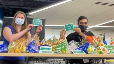 Two students preparing care packages hold up thank-you notes