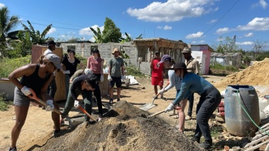 A group of people working outdoors, some holding shovels or digging