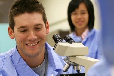 Two researchers smiling whie using microscopes