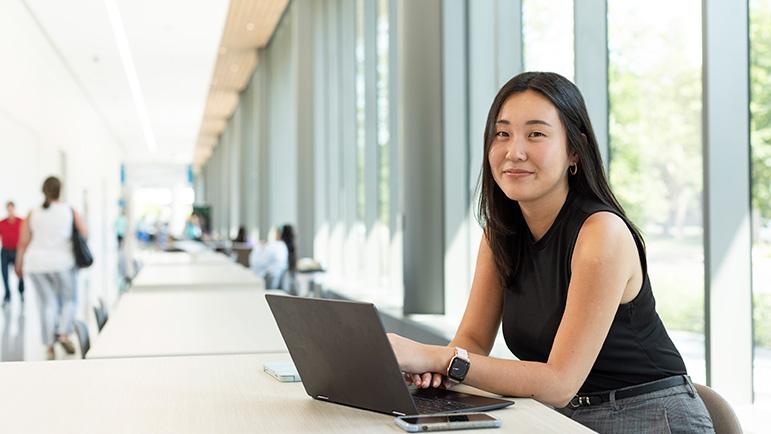 Ye Rim Noh sits in front of a laptop in a windowed, sunlit room on campus.