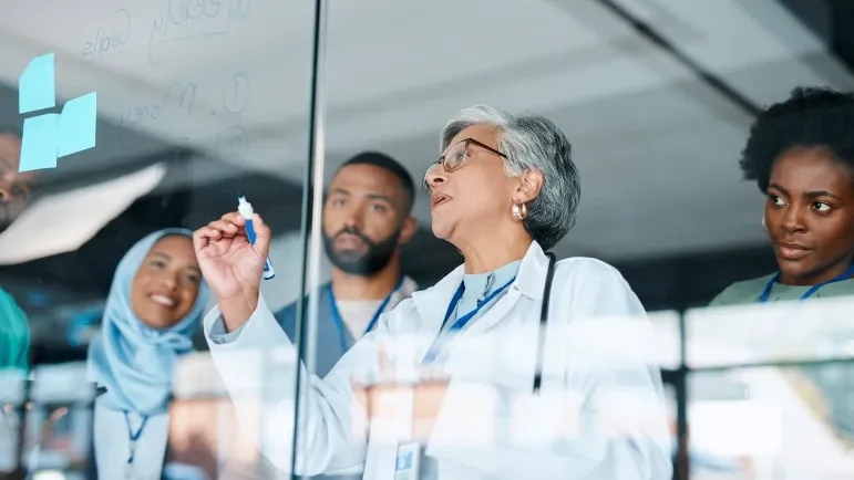 A group of health care providers in conference making notes on an erasable board