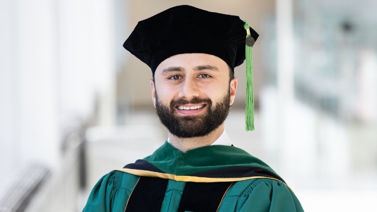 Andrew Mohama will serve as Rush University's 54th Commencement Ceremony student speaker. He is smiling in his green, gold and black regalia.