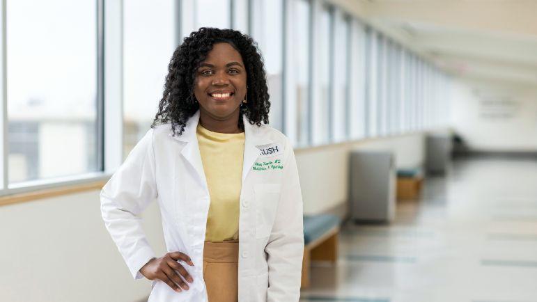 A smiling doctor wearing a white coat in front of windows in a hospital corridor